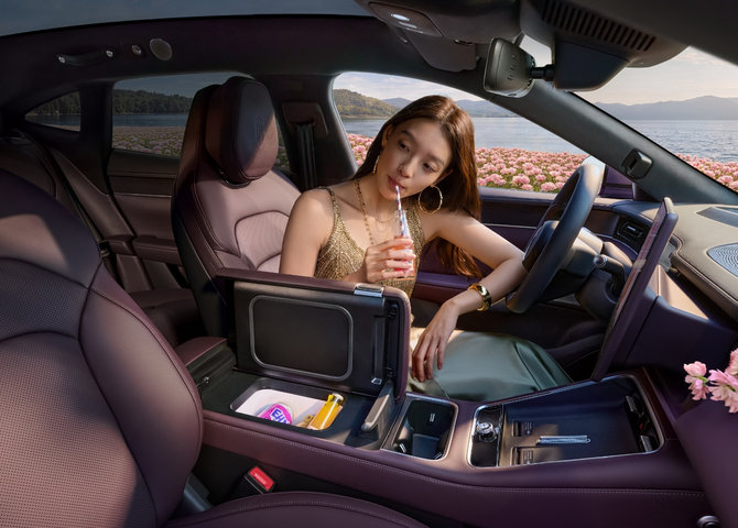 A user sitting in the Shangjie Z7-Z7T driver's seat drinking a beverage, showing the car's onboard air-cooled fridge.