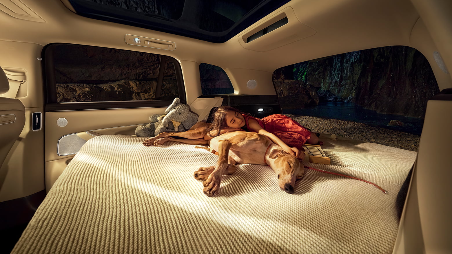A little girl holding a dog and sleeping on the unfolded king-bed of the AITO M8 in White Sand Apricot