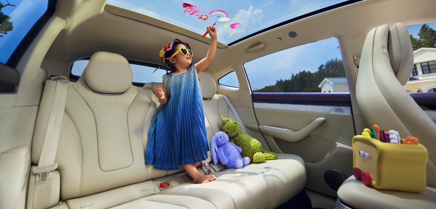 A little girl standing barefoot on the rear seat, drawing on the sunroof, showing the comfortable feel of the Luxeed R7's Silk Cloud Seats