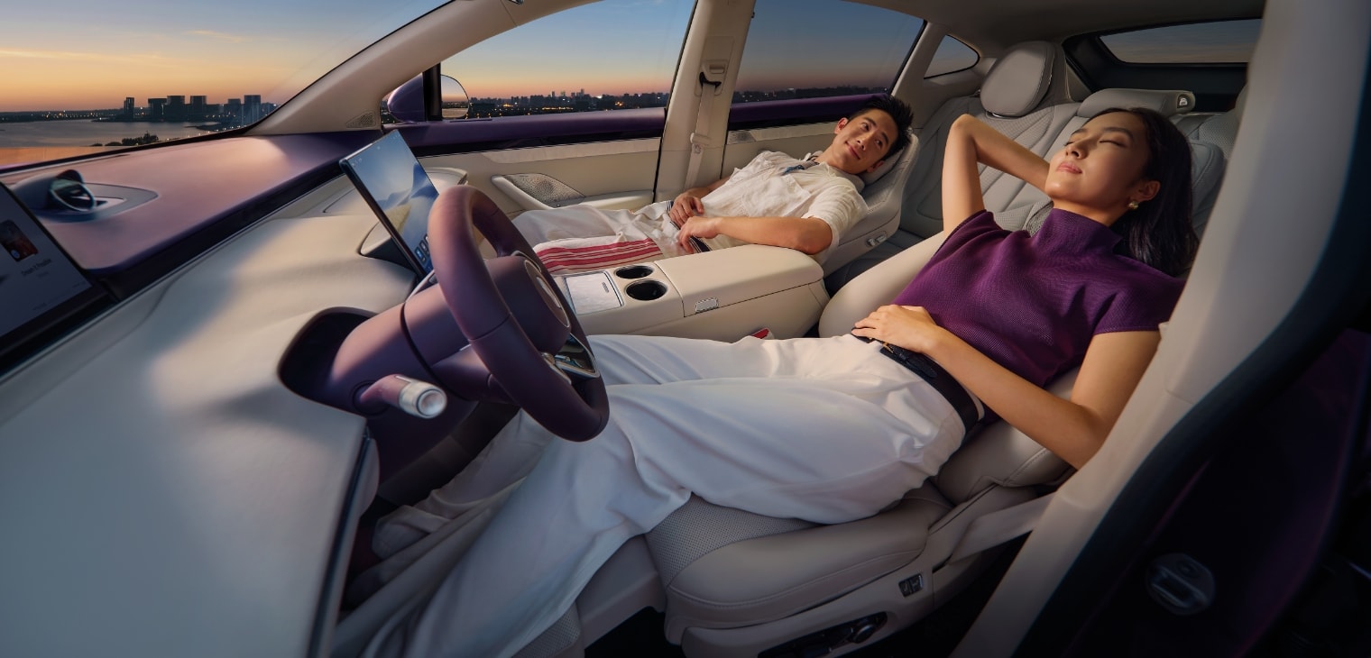 Two people reclining comfortably in the front seats, showing the Luxeed R7's dual zero-gravity seats for driver and front passenger