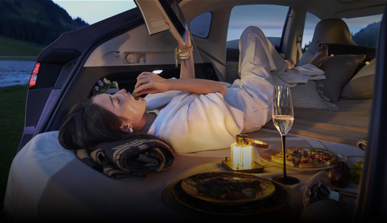 A woman lying freely in the rear enjoying reading time, showing the Luxeed R7's versatile feature of folding the rear seats flat into a bed-car