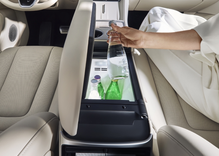 A woman opening the cooler/warmer box from the passenger seat and taking out a drink, showing the Luxeed R7's onboard cooler/warmer box function